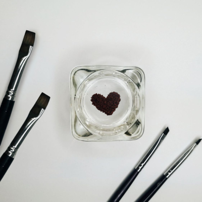 Cinco pincéis de maquilhagem e recipiente de vidro com grãos em forma de coração