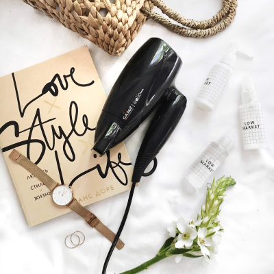 Secador de cabelo preto, frascos brancos, relógio castanho, argolas douradas, flor branca e livro com texto Love Style Life