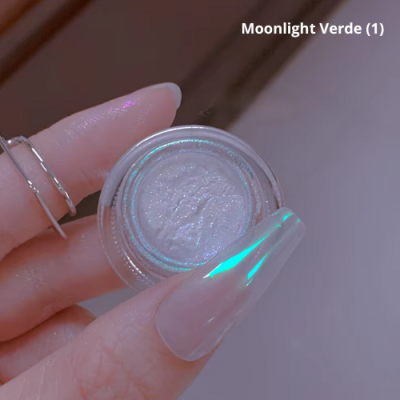 Pequeno frasco de pigmento brilhante branco com reflexos verdes segurado por mão feminina com unhas longas e transparentes