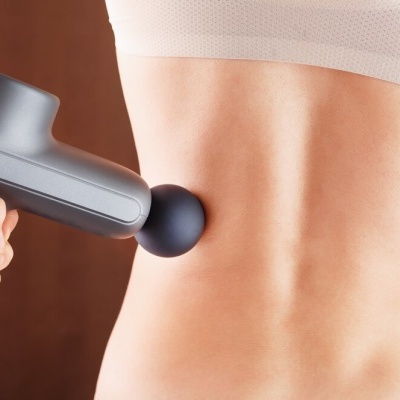 Massageador portátil cinza a ser usado na zona lombar de uma pessoa.