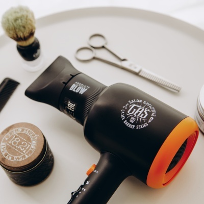 Secador de cabelo preto com detalhes laranja e texto branco numa bandeja branca com acessórios de barbear