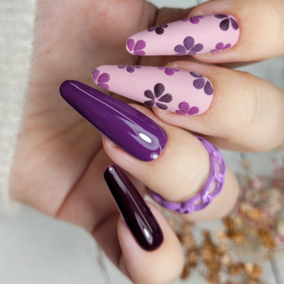Unhas com verniz roxo e rosas decoradas com flores roxas e anel roxo translúcido
