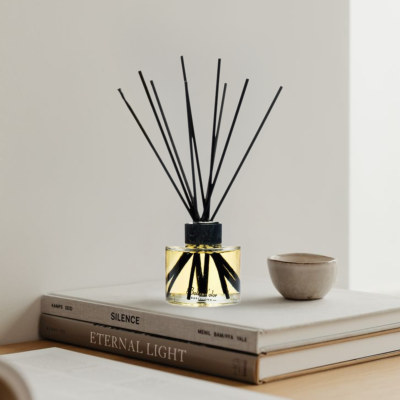 Difusor de fragrância com varas pretas em vidro transparente sobre livros e ao lado de tigela de cerâmica