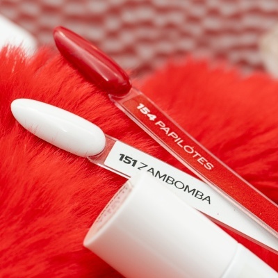 Amostras de verniz de unhas vermelho e branco em palitos sobre superfície vermelha felpuda