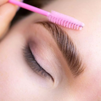 Escova rosa a pentear sobrancelha castanha em pele clara com olhos fechados.