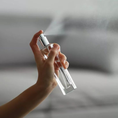 Frasco de spray transparente com tampa prateada sendo usado numa mão