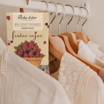 Mini sachet perfumado frutos rojos pendurado em cabides de madeira com roupas claras ao fundo