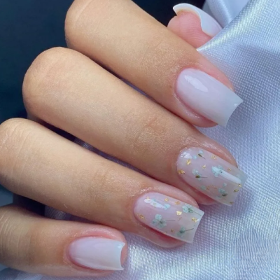 Mão com unhas decoradas em rosa suave com flores brancas e detalhes dourados