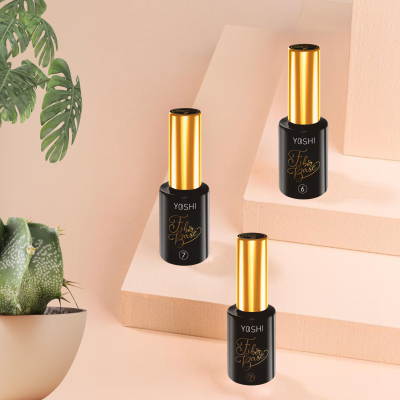 Três frascos de verniz YOSHI com tampas douradas e texto dourado sobre fundo rosa com planta