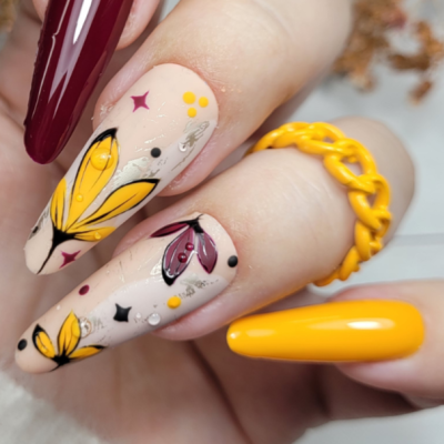 Unhas decoradas com esmalte creme, amarelo e vinho e anel amarelo em corrente