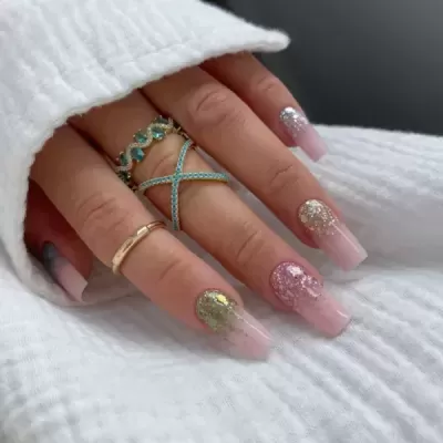 Mãos femininas com unhas cor de rosa e glitter com anéis dourados