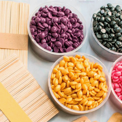 Pastilhas de cera depilatória coloridas em recipientes plásticos com palitos de madeira