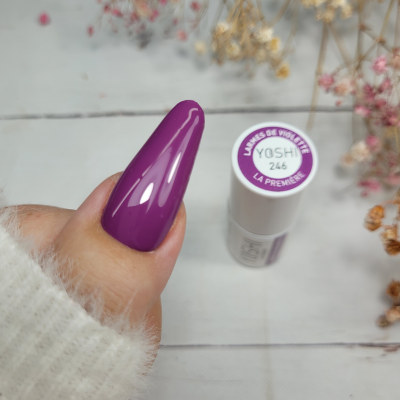 Unha com verniz roxo próximo a frasco branco de verniz rotulado