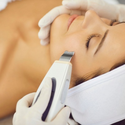 Tratamento facial com dispositivo ultrassónico e mãos com luvas brancas