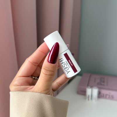 Mão com unhas vermelhas segurando frasco branco de cosmético Yooshi Lacquer