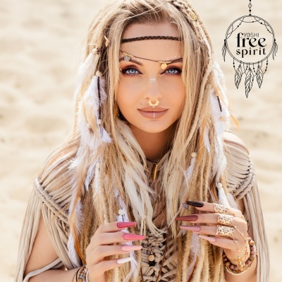 Mulher boémia com cabelos trançados, penas, joias douradas e unhas pintadas num fundo de areia