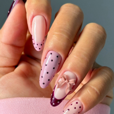 Unhas decoradas com verniz rosa claro, bolinhas pretas e laço 3D no anelar