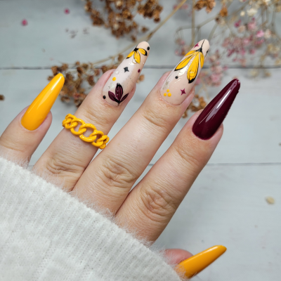 Unhas pintadas amarelo e bordô com desenhos florais e anel amarelo de corrente