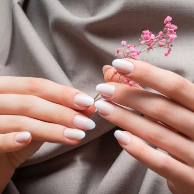 Mãos com unhas esmaltadas em branco segurando flores cor de rosa sobre tecido cinza