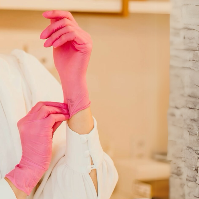 Luvas descartáveis cor-de-rosa sendo colocadas numa mão com camisa branca