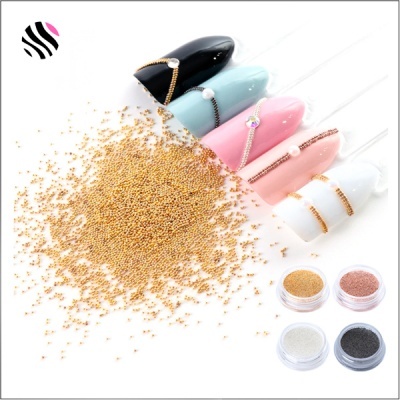 Unhas postiças coloridas com decoração dourada e pérolas junto a microesferas douradas e recipientes de pigmentos.