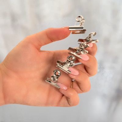 Mão feminina segurando grampos de metal prateados com mola
