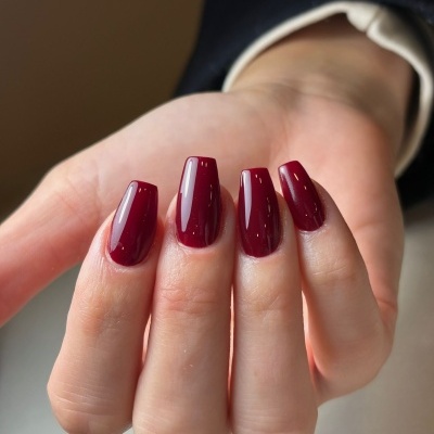 Unha vermelha vinho com acabamento brilhante em mão de pele clara
