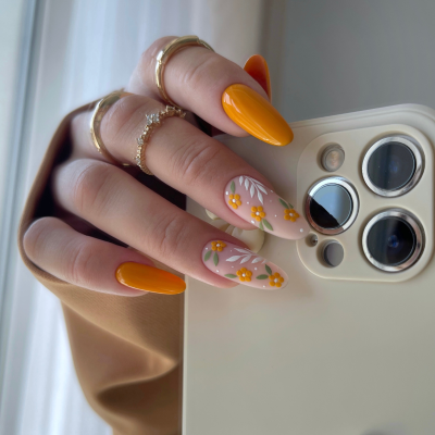 Unhas decoradas com design floral e anéis dourados segurando telemóvel branco