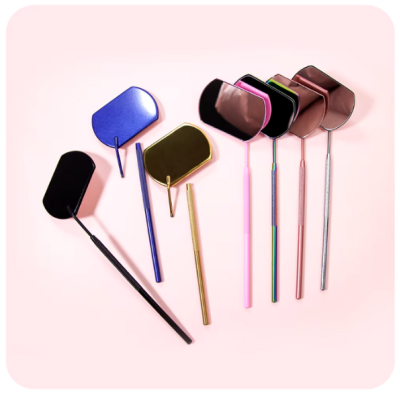 Espelhos retangulares pequenos com cabo fino em várias cores metálicas sobre fundo rosa claro.