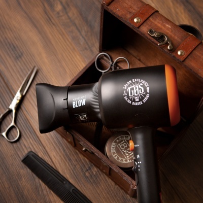 Secador de cabelo preto com detalhes laranja dentro de caixa de madeira com tesoura, pente e pomada.
