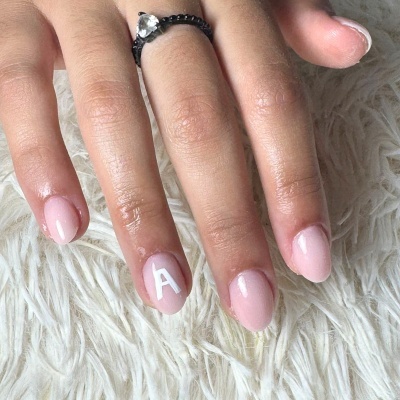 Mão com unhas cor-de-rosa e letra A branca numa unha, com anel preto, sobre tecido felpudo branco