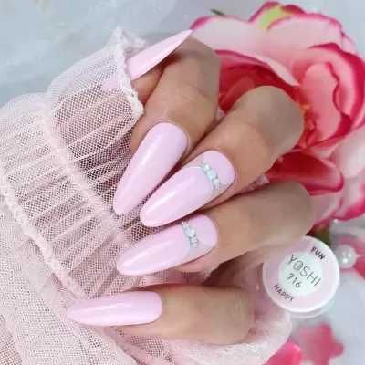 Unhas compridas pintadas de rosa claro com cristais, tecido branco rendado e fundo com flor rosa e verniz YOSHI 716
