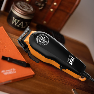 Máquina de cortar cabelo preta e laranja com lâmina metálica sobre mesa de madeira com cera, caderno e escova