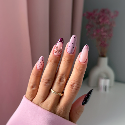 Unhas decoradas com padrões de bolinhas e laço 3D em tons rosa e preto