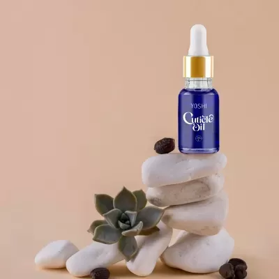 Frasco azul de óleo para cutículas sobre pedras brancas com suculenta e grãos de café