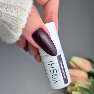 Frasco branco de verniz para unhas YOSHI Jelly Hybrid Paixão de Mutum com mão segurando e fundo com flores amarelas.