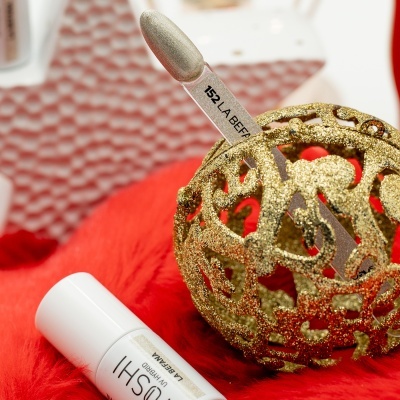 Paleta de verniz dourada e branca com código 152 LABEL FORT numa esfera dourada sobre tecido vermelho felpudo e tubos brancos