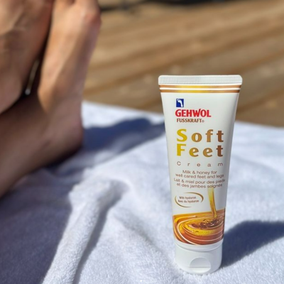 Creme para pés Gehwol Soft Feet em tubo branco sobre toalha branca com pés ao fundo
