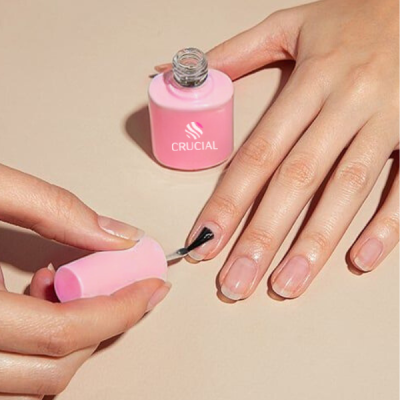 Mãos a aplicar verniz preto em unhas com frasco rosa ao fundo