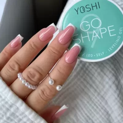 Unhas de gel rosa e branco com anéis de pérolas ao lado de um pote de gel