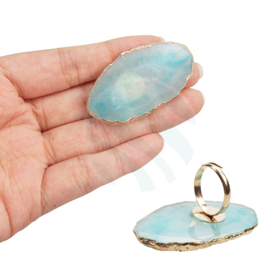 Anel com suporte em pedra azul translúcida com bordas douradas e aro metálico num fundo branco