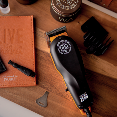 Aparelho de corte de cabelo preto e laranja com acessórios e caderno laranja sobre mesa de madeira
