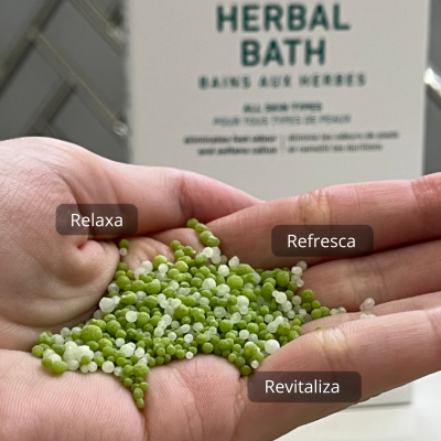 Pérolas verdes e brancas nas mãos com embalagem de produto de banho ao fundo