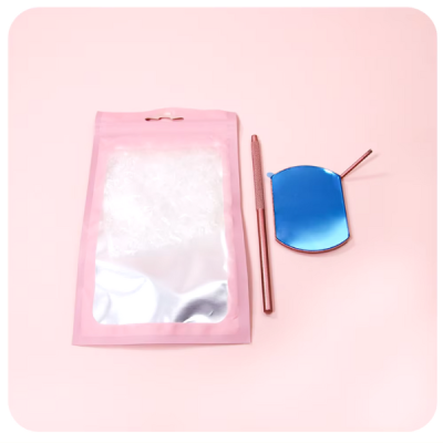 Saco plástico rosa translúcido, ferramenta metálica rosa e espelho hexagonal pequeno com moldura rosa