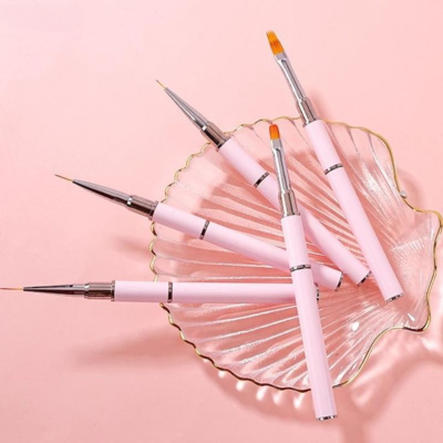 Cinco pincéis para unhas rosa numa concha de vidro sobre fundo rosa