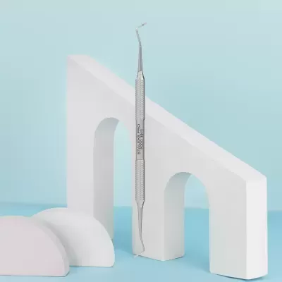 Instrumento dental metálico DUPIXES nº 006 entre formas decorativas brancas sobre fundo azul claro