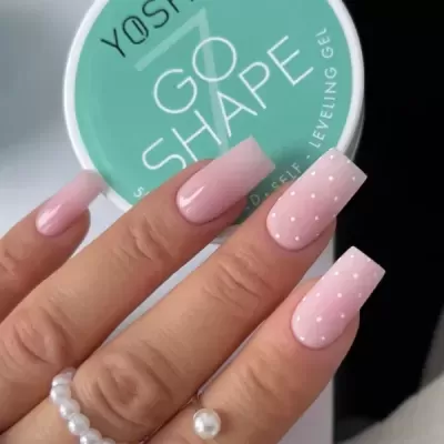 Mãos com unhas postiças rosa claro e bolinhas brancas segurando frasco verde de gel