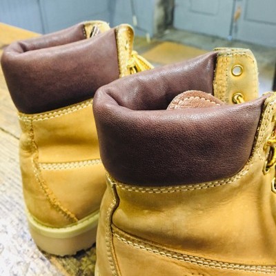 Botas amarelo mostarda com colarinhos em couro castanho escuro vistas em chão de madeira