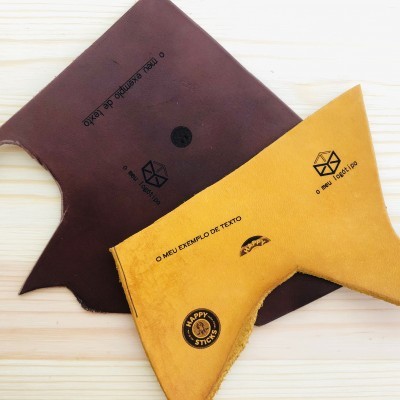 Dois pedaços de couro triangular em cores castanho escuro e amarelo com inscrições em preto sobre superfície de madeira clara.