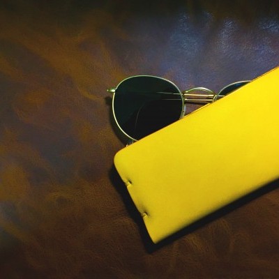 Óculos de sol com armação dourada e capa amarela sobre fundo castanho